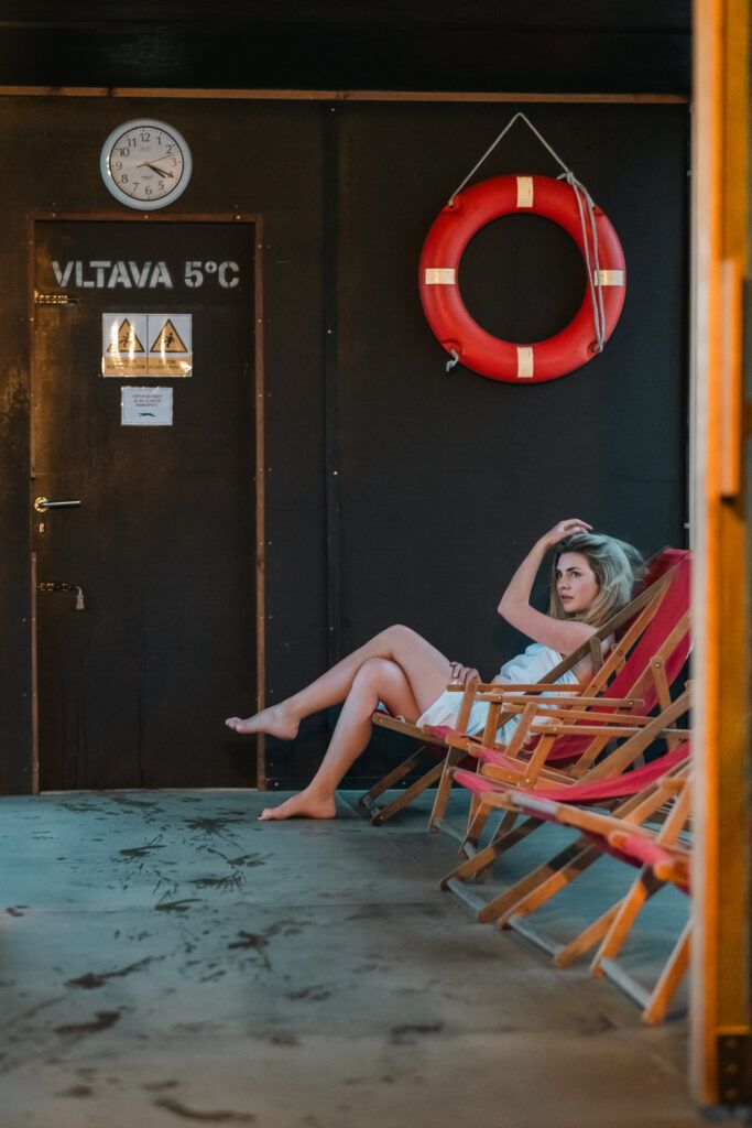 Odpočívárna s lehátky, záchranný kruh a dveře s nápisem Vltava 5 °C